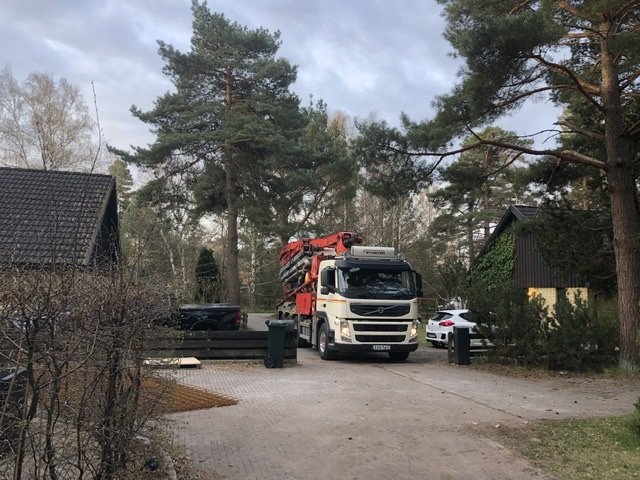 Lastbil med kran på en uppfart framför hus, indikerar starten på ett byggprojekt.