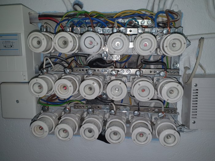 Äldre elektriskt skåp med säkringar och tråddragning, bi-ledare kopplad till jord, och blå kabel till säkring.