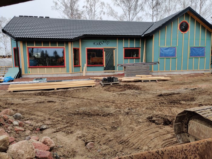 Hus under renovering med nytt tak, skyddade fönster och byggmaterial framför.