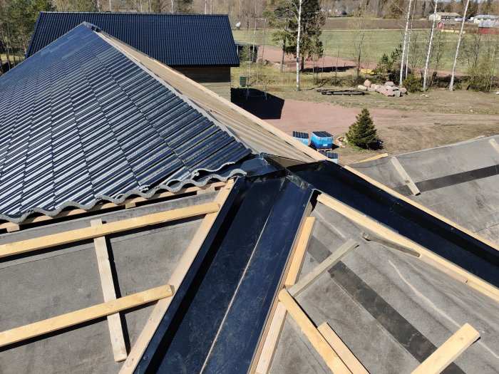 Ränndalsplåtar monterade på husnock med pågående takarbete, läkt och halvt lagt taktegel.