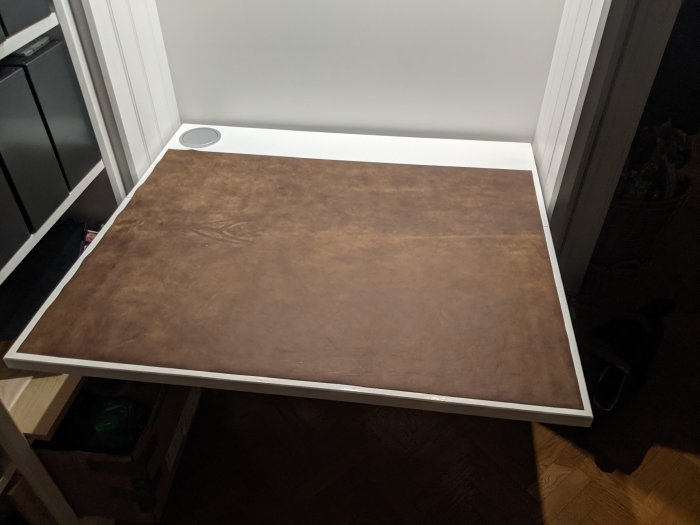 Gammal plastskiva med brun yta använd som hyllplan eller arbetsyta, placerad på ett vitt bord i ett rum.