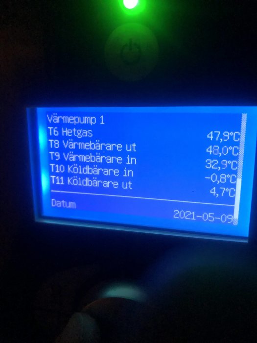 Skärm på värmepump som visar temperaturvärden och status, med felkod och datum.