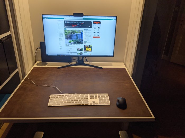 Skrivbord med datorbildskärm, tangentbord och mus, ordnade sladdar och en infräst laddare på höger sida.