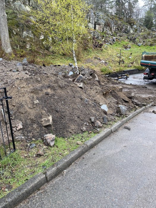 Hög med jord, lera och stenar bredvid en väg och lastbil i bakgrunden.