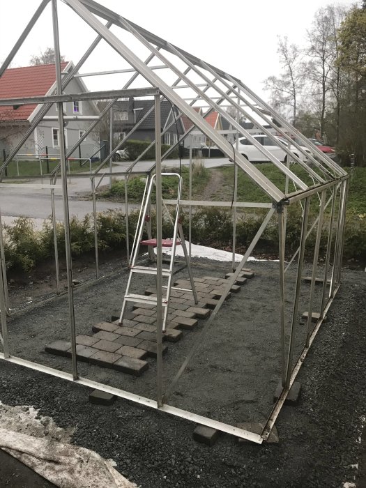 Ett omonterat äldre växthus stomme utan glas med unika hörnbeslag på en stenlagd grund.
