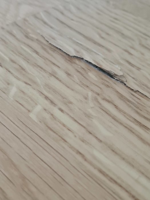 Stor skada på parkettgolv med ett uppdraget jack i träet mot en suddig bakgrund.