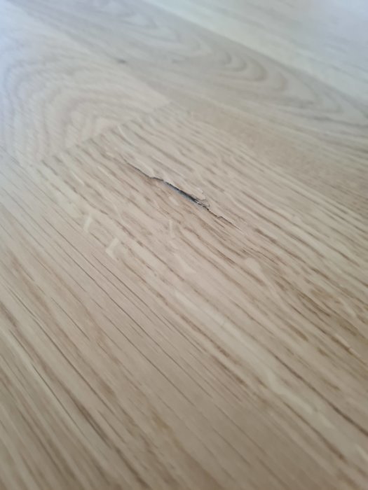 Jack i parkettgolv, närbild på skadan där träfibrerna är synligt uppristade.