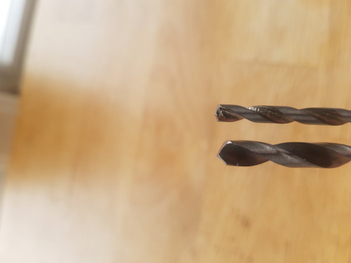 Två metallborrar med synlig ocentrering och slitage på ett träunderlag.