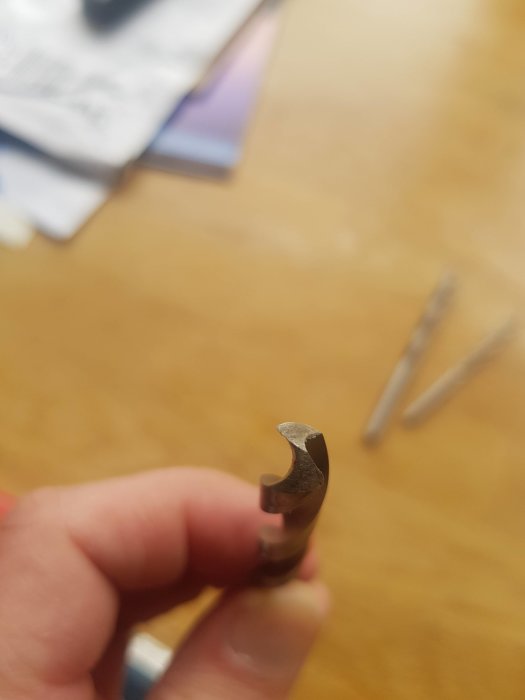 Närbild på en hand som håller en ocentrerad metallborr med synliga defekter.