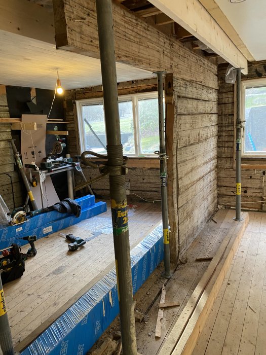 Renoveringsarbete med stämpar och nyinstallerad limträbalk i ett hus under ombyggnad.