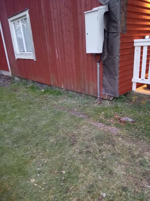 Utgrävning mark på tomten nära timmerhusets vägg för fiberinstallation, med synlig kabelförläggning och husgrund.