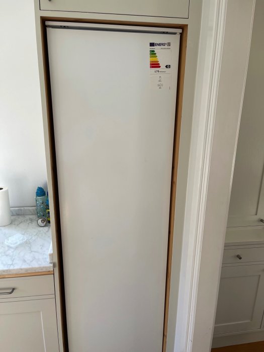 Inbyggt kylskåp utan synliga gångjärn monterat i vit kökssnickeri.