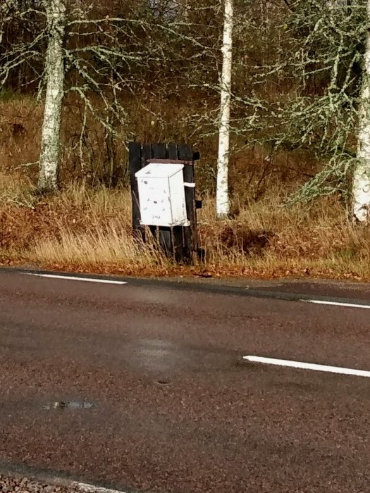 Hemmasnickrad stor postlåda vid en väg, ser instabil och väderskadd ut med snö och regninträngning.