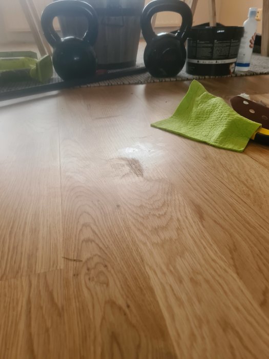 Nyslipat trägolv med synlig reparation, omgivet av slipmaterial, hantlar och rengöringsflaska.
