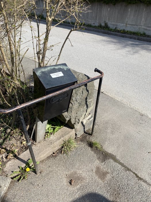 Svart brevlåda vid trottoarkant med lappen "Ingen reklam tack".