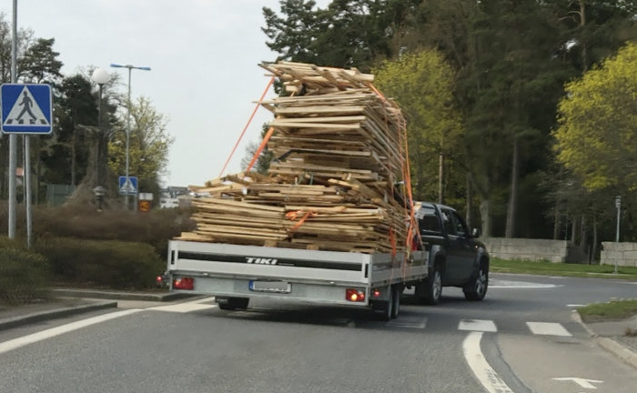 Lastbil med överlastad släpvagn fylld med plankor på en stadsgata.