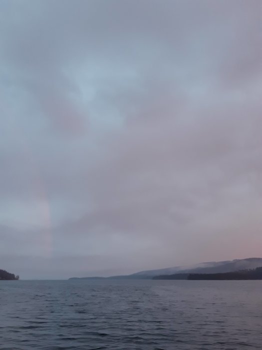 Pastellfärgad himmel under solnedgång med svaga rosa toner som reflekterar över en sjös vattenyta.