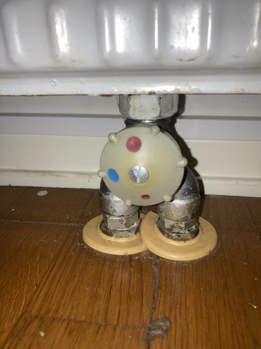 Ett vitt och blått vred på en radiatorventil, fastsatt vid golv på ett trägolv, ser gammalt och oanvänt ut.