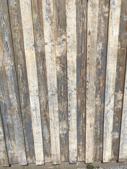 Vertikala träplankor på ett garage med flagande blå linoljefärg och exponerat trä.