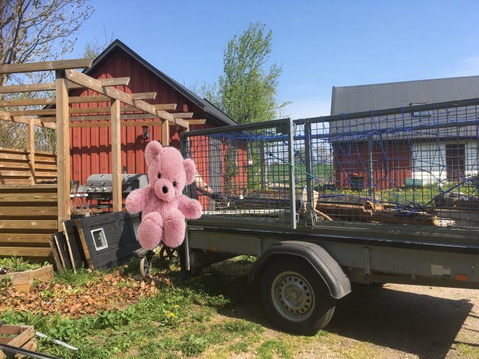 Släpvagn lastad med gamla dörrar och bråte från renovering, rosa gosedjur i förgrunden, utomhusmiljö.