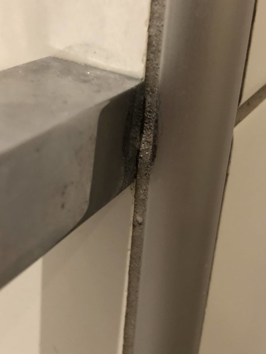 Pappershållare monterad på kakelvägg med synlig skada i fog och antydan till orange missfärgning.