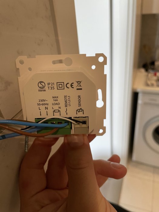 Elkoppling av golvvärmetermostat med bruna och blåa kablar sammankopplade, hålls av en hand.