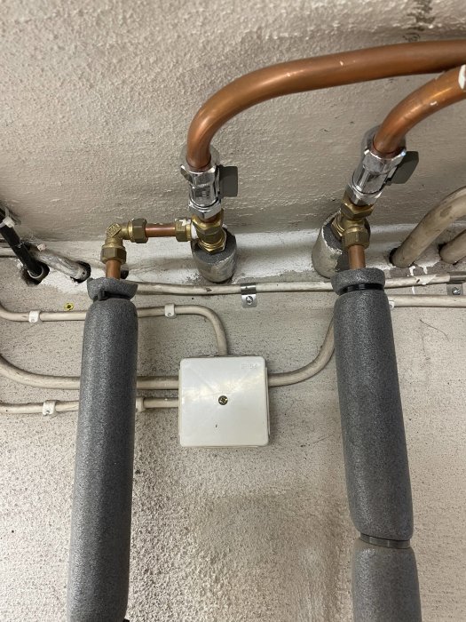 Rörinstallation på vägg med T-kopplingar och ventiler för radiator, isolering och en eldosa.