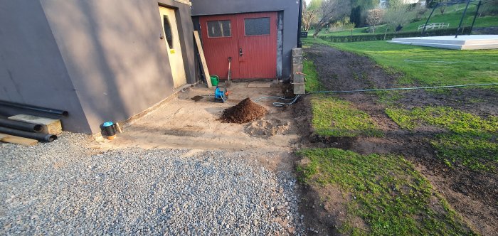 Renoverad yta utanför garage med borttagen betongplatta, sandbädd, kross och gräns mot gräsmatta.