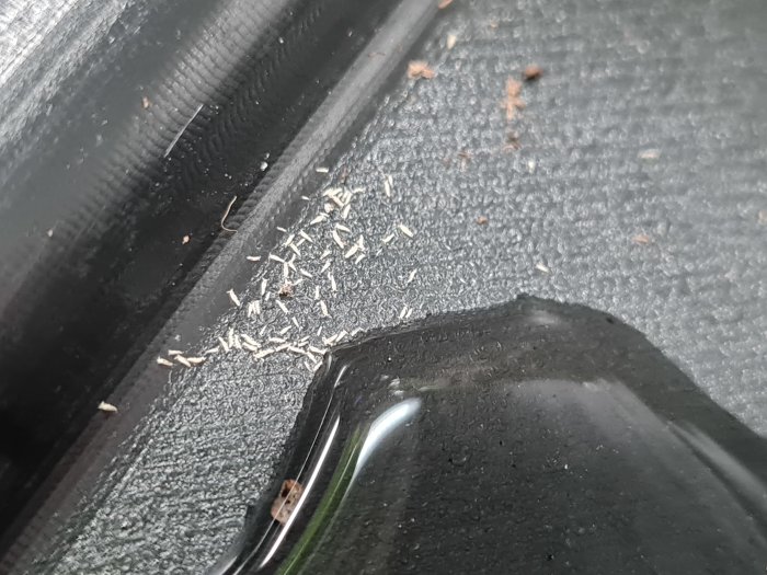 Närbild på små spån och skräp i hörnet av en svart yta med en suddig vattendroppe i förgrunden.