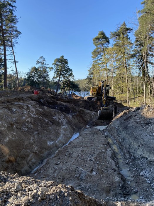 Grävmaskin mitt i markarbeten med öppen schaktgrop och synliga bergpartier på en byggarbetsplats.