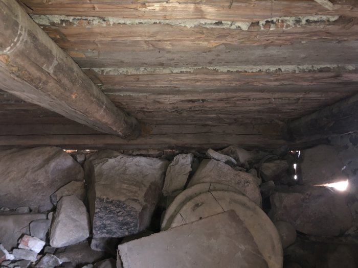 Gammal husgrund med stenar och träbjälkar, synliga tecken på slitage och ålder, under sommarhus från 1800-talet.