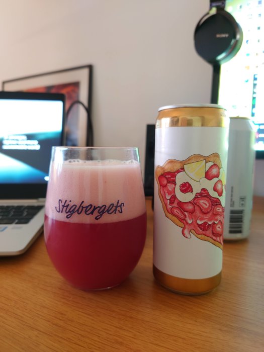 Ett glas med rosa öl och en burk med illustration av pizza, framför en datorskärm.