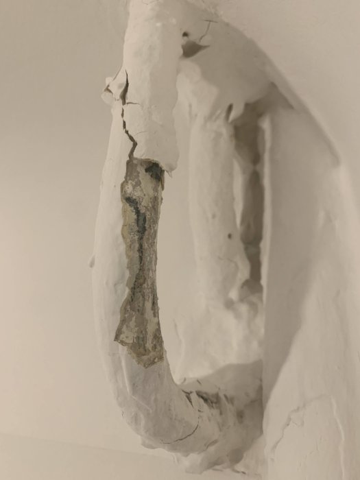 Ett rör i taket med flagande och sprucken vit färg som blottar det underliggande materialet.