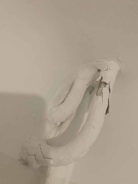 Vitmålat rör med flagande och sprucken färg mot en vit bakgrund.