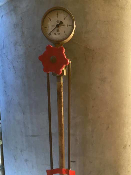 Tryckmätare på noll på en vattenpumpstank med röd ventil och otydligt rör.