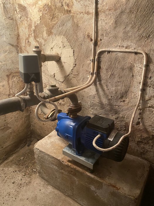Vattenpump och rörinstallation i källare med tryckmätare som visar 0.