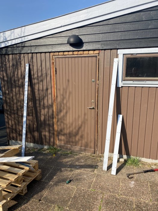 Nyinstallerad garagedörr på ett hus, gamla fodret synligt, byggmaterial framför.