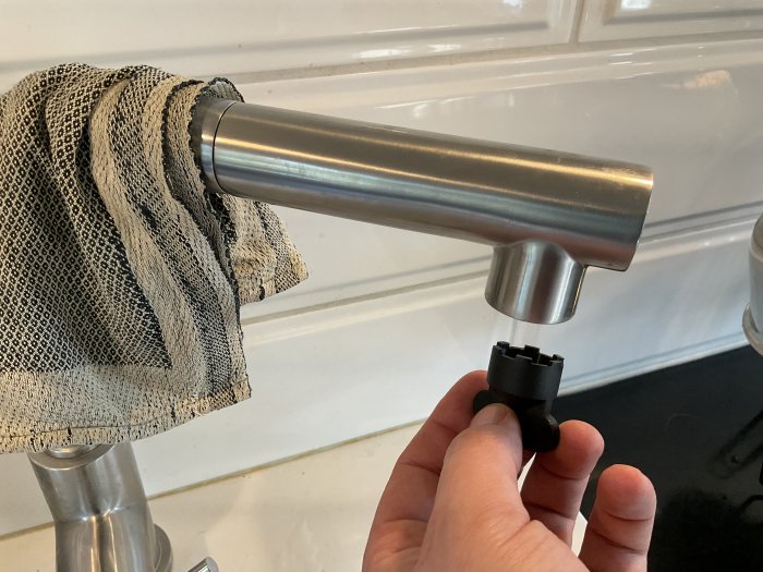 Hand håller ett verktyg för att skruva ur en perlator från en strandblandare vid ett vitt kakel.