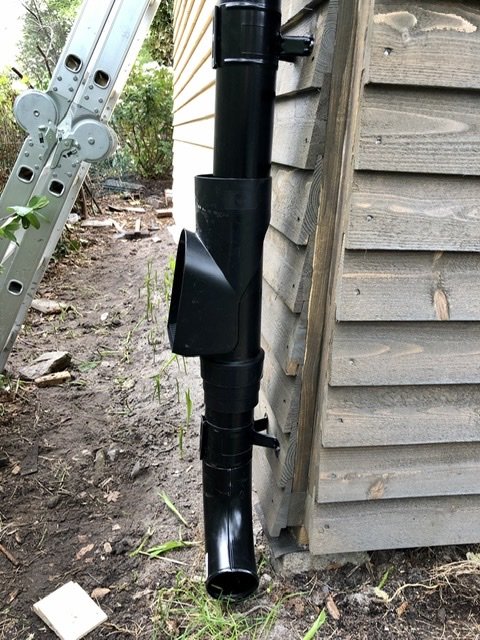 Nyinstallerad svart hängränna på trähus med renstratte och rör, bredvid stege.