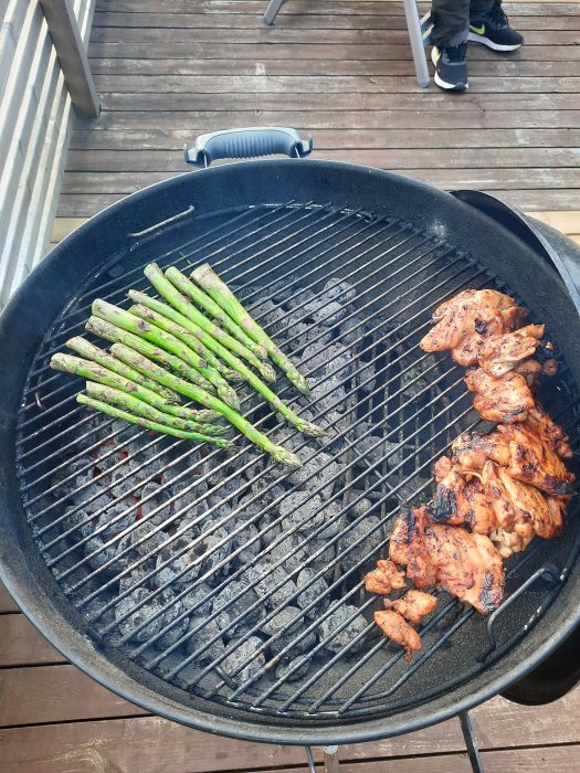 Grillad sparris och kyckling på ett kolgrillgaller, med träaltan i bakgrunden.