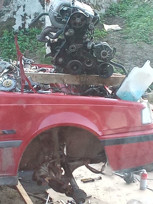 Delvis demonterad röd Volvo 460 med motor och delar liggande framför bilen under renoveringsarbete.