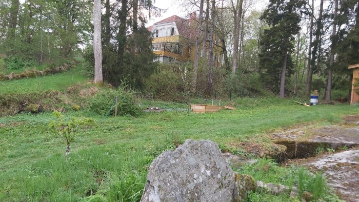 Ojämn gräsmatta med mindre backar och en grusväg framför en gulfärgad villa i bakgrunden.