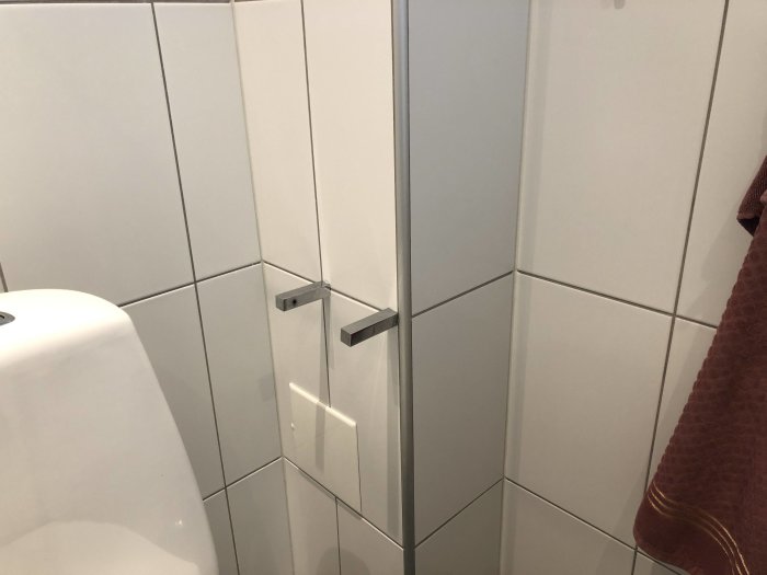 Duschhörna med vita kakelväggar och en glasdörr där en lucka finns strax under en dörrhandtag.