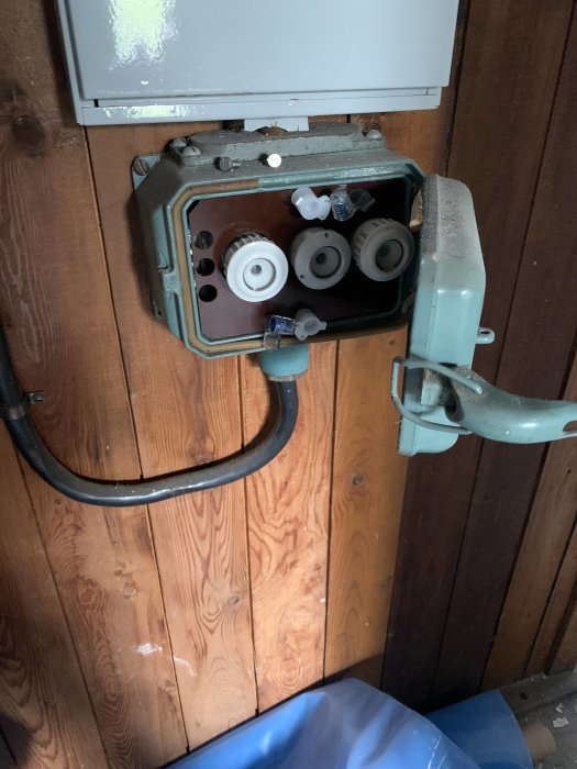 Öppet eluttag med 3 faser synligt i en väggmonterad kabelkanal mot en trävägg.