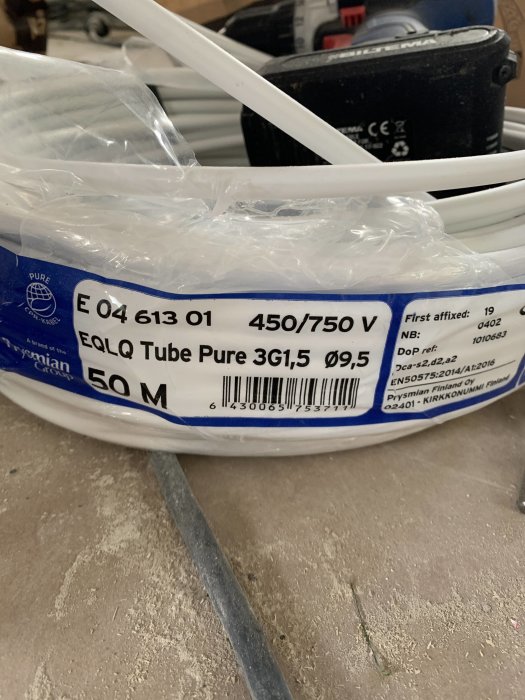 Rulle med vit 3g1,5 elektrisk kabel märkt "EQLQ Tube Pure 3G1,5" och längdangivelse på golv.