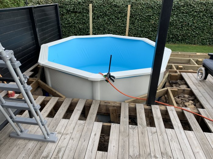 Omonterad pool på träplattform med avmonterade plankor och byggmaterial runtomkring.