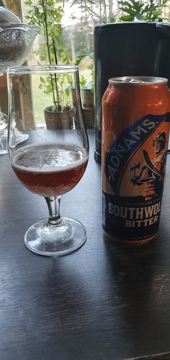 En burk Adnams Southwold Bitter och ett halvfullt glas med öl på ett bord.