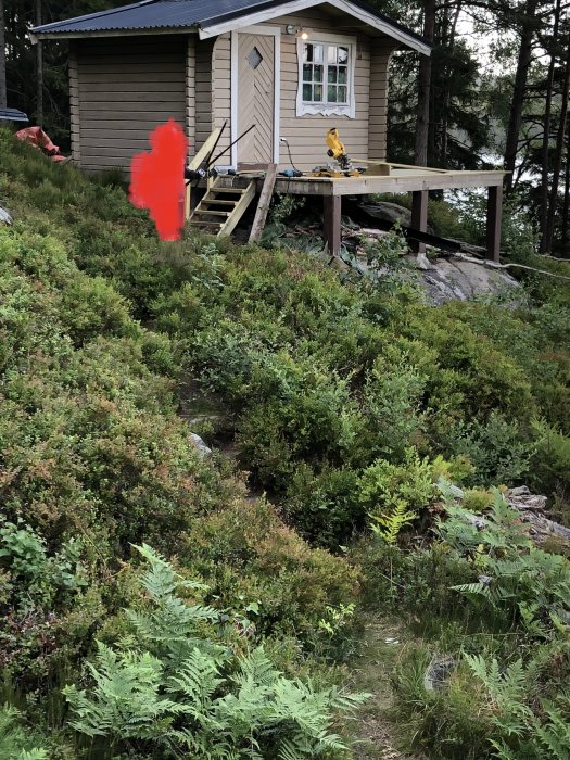 Nybyggd altan med färsk trall utan staket vid stuga med utsikt över skog.