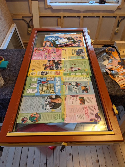 Nystruken fönsterbåge i rött liggande på golvet täckt av tidningspapper, med målartillbehör runtomkring.