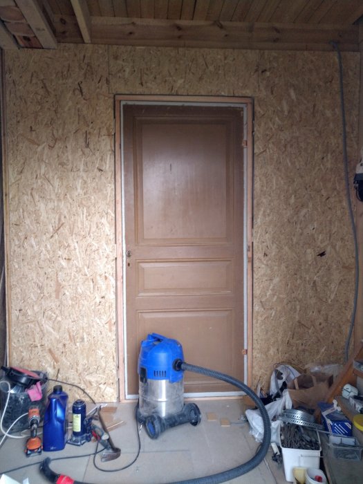 Renoverat rum med nygipsade väggar, reglat innertak och installerad dörrkarm bland byggmaterial och verktyg.